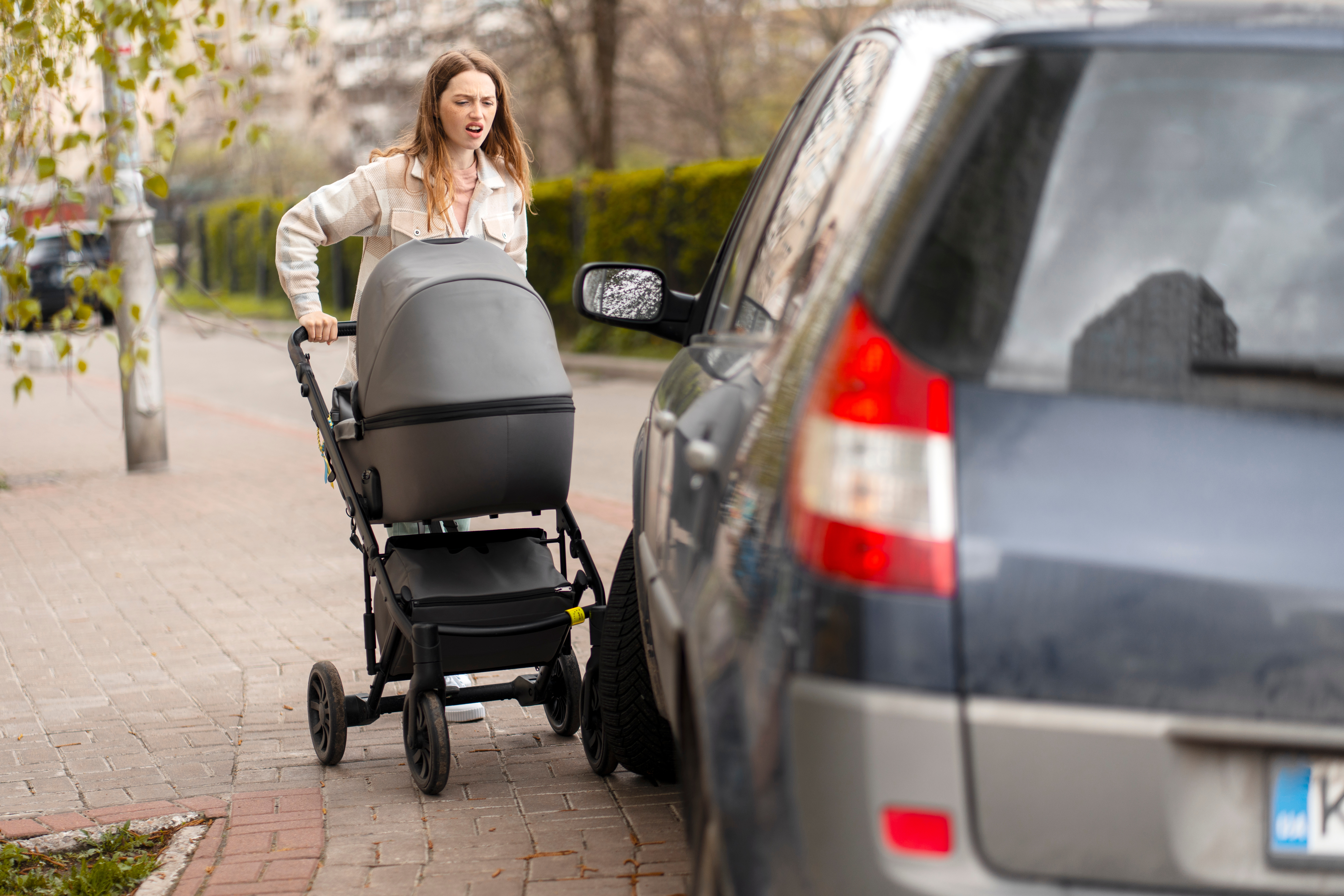 Ein geparktes Fahrzeug blockiert den Fußweg, eine Frau mit Kinderwagen kann nicht passieren