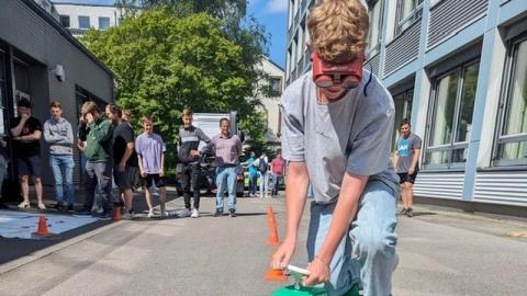 Ein Jugendlicher fährt auf einem Bobbycar um rote Hütchen. Er trägt eine sogenannte Rauschbrille, die den Zustand unter Alkoholkonsum darstellen soll.