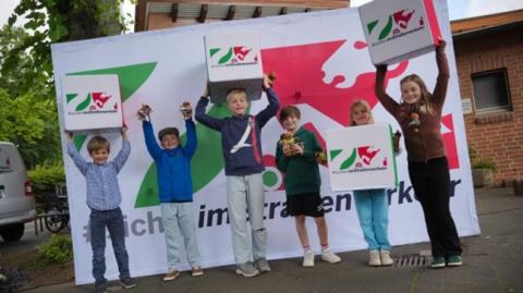 Schulkinder vor einer Wand mit dem Logo der NRW Initiative - #sicherimStraßenverkehr