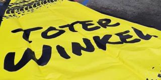 Eine gelbe Plane liegt auf dem Boden. Die Aufschrift "Toter Winkel" ist zu lesen, im oberen Bildrand sind Reifenabdrücke zu sehen